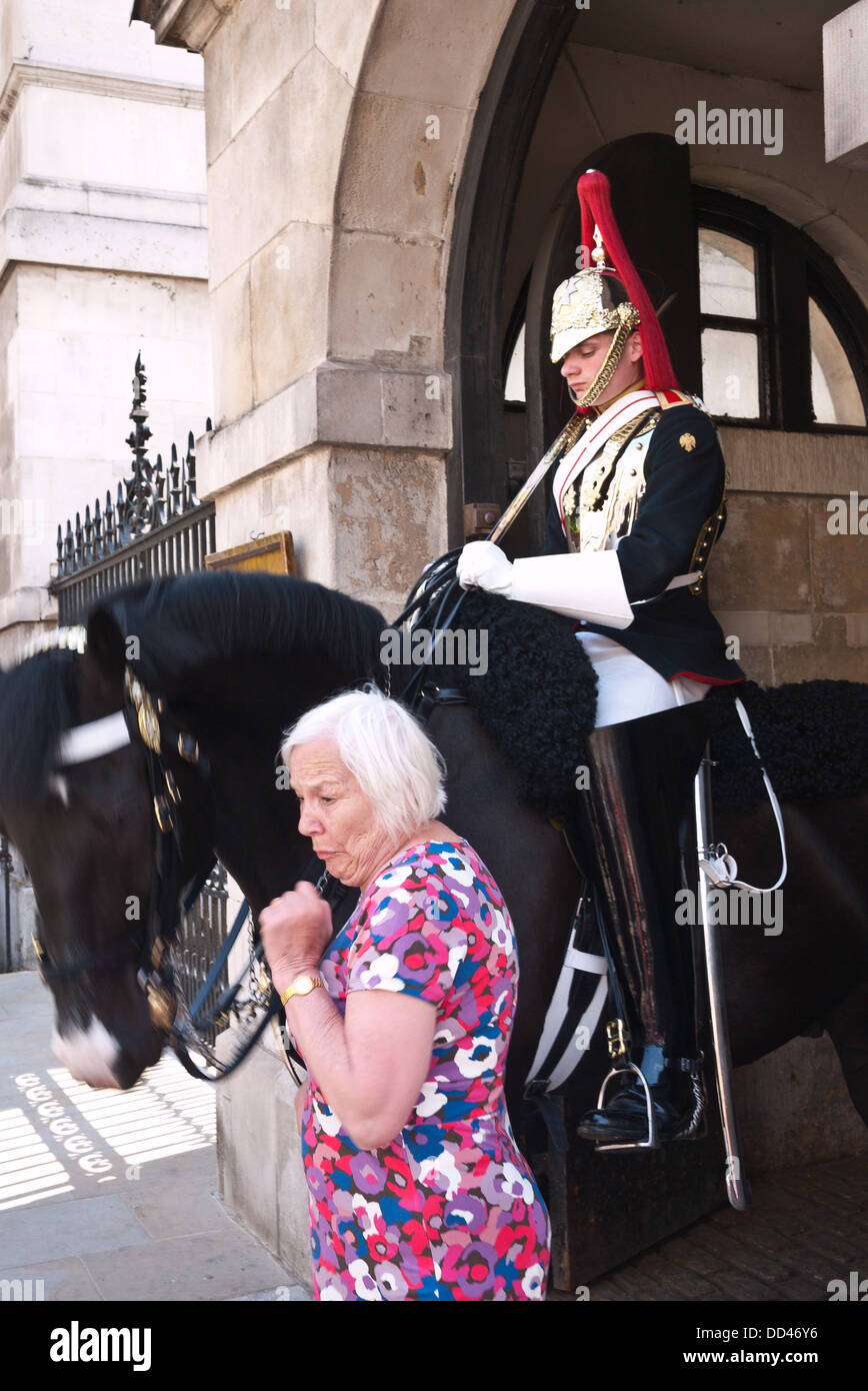 A woman flinches as a horse suddenly makes her jump whilst posing for a picture in front of the tourist attraction in London. Stock Photo