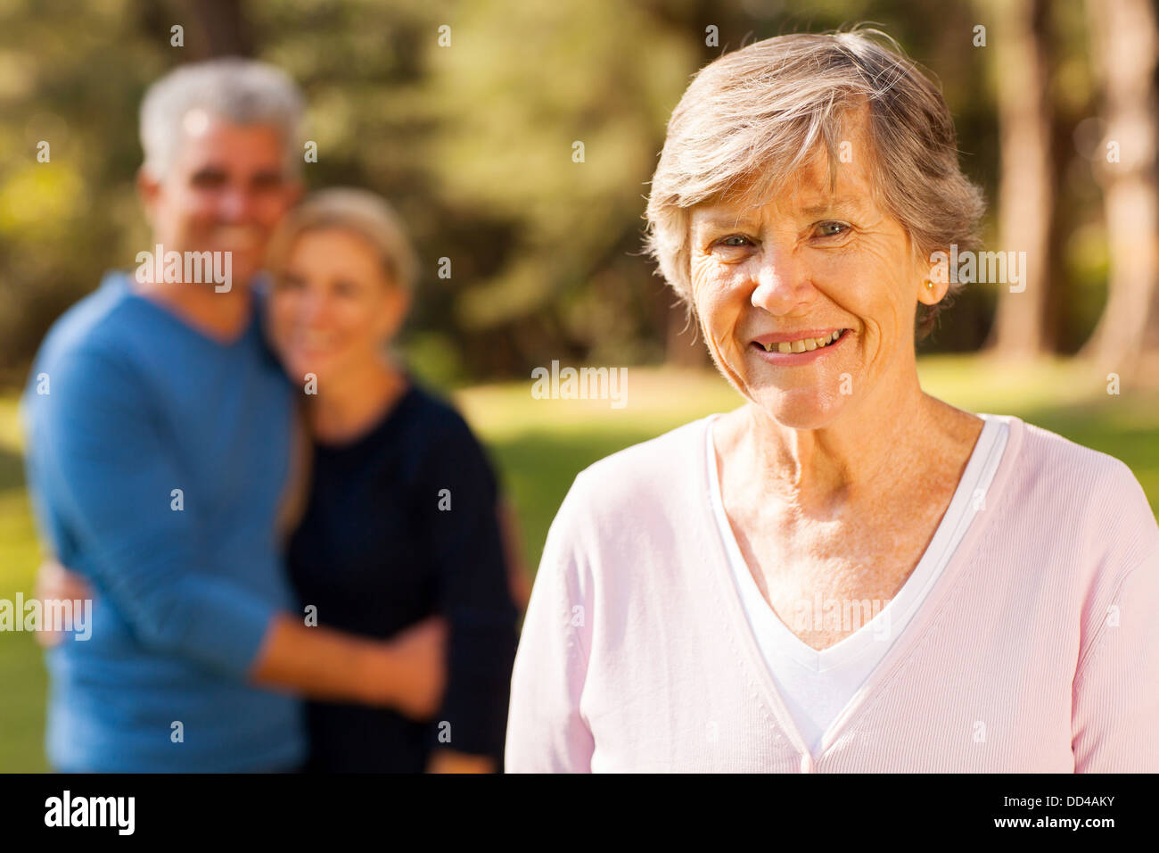 portrait of senior woman in front of middle aged son and daughter-in-law outdoors Stock Photo