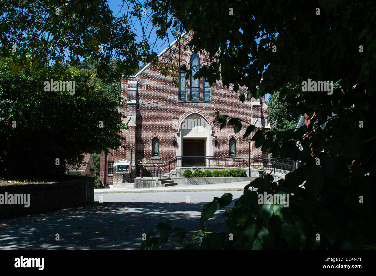 A brown brick church in a small town on a small street on a hilltop with trees framing the church. Stock Photo