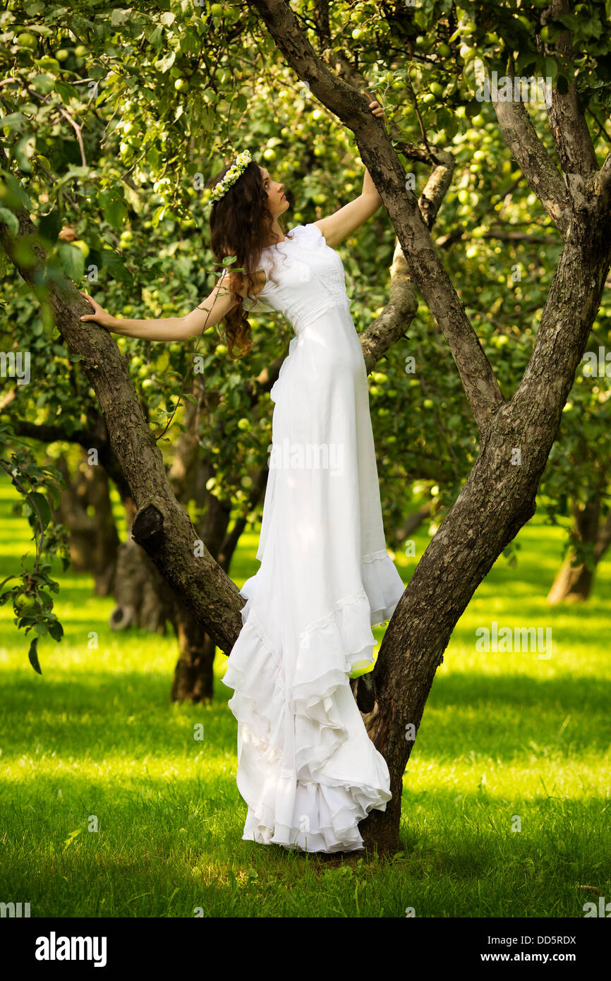 Woman in a long white dress sitting on the grass in the apple orchard ...