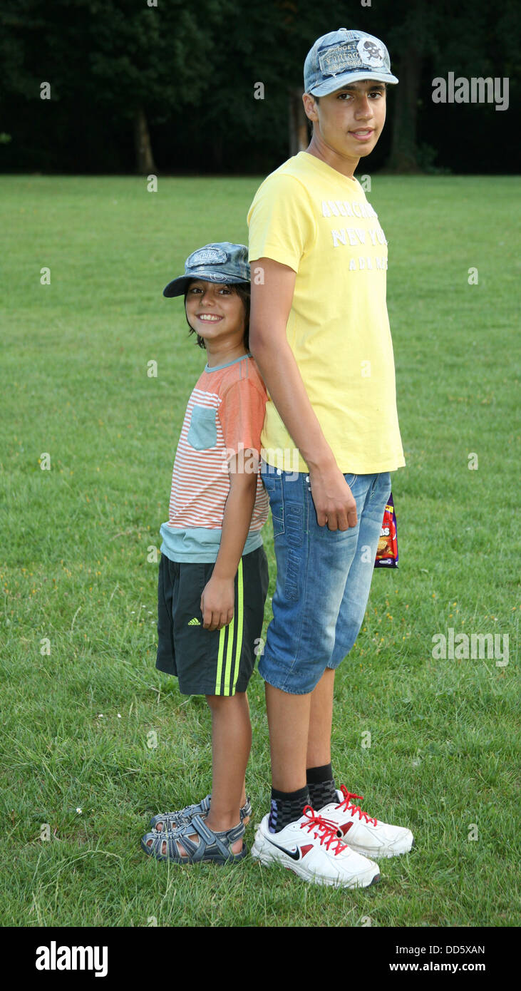 Portrait of smiling brothers in baseball caps standing back to back in park Stock Photo