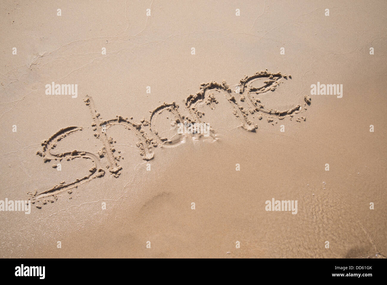 The word "shame" written in the sand, being washed away by a wave. Stock Photo