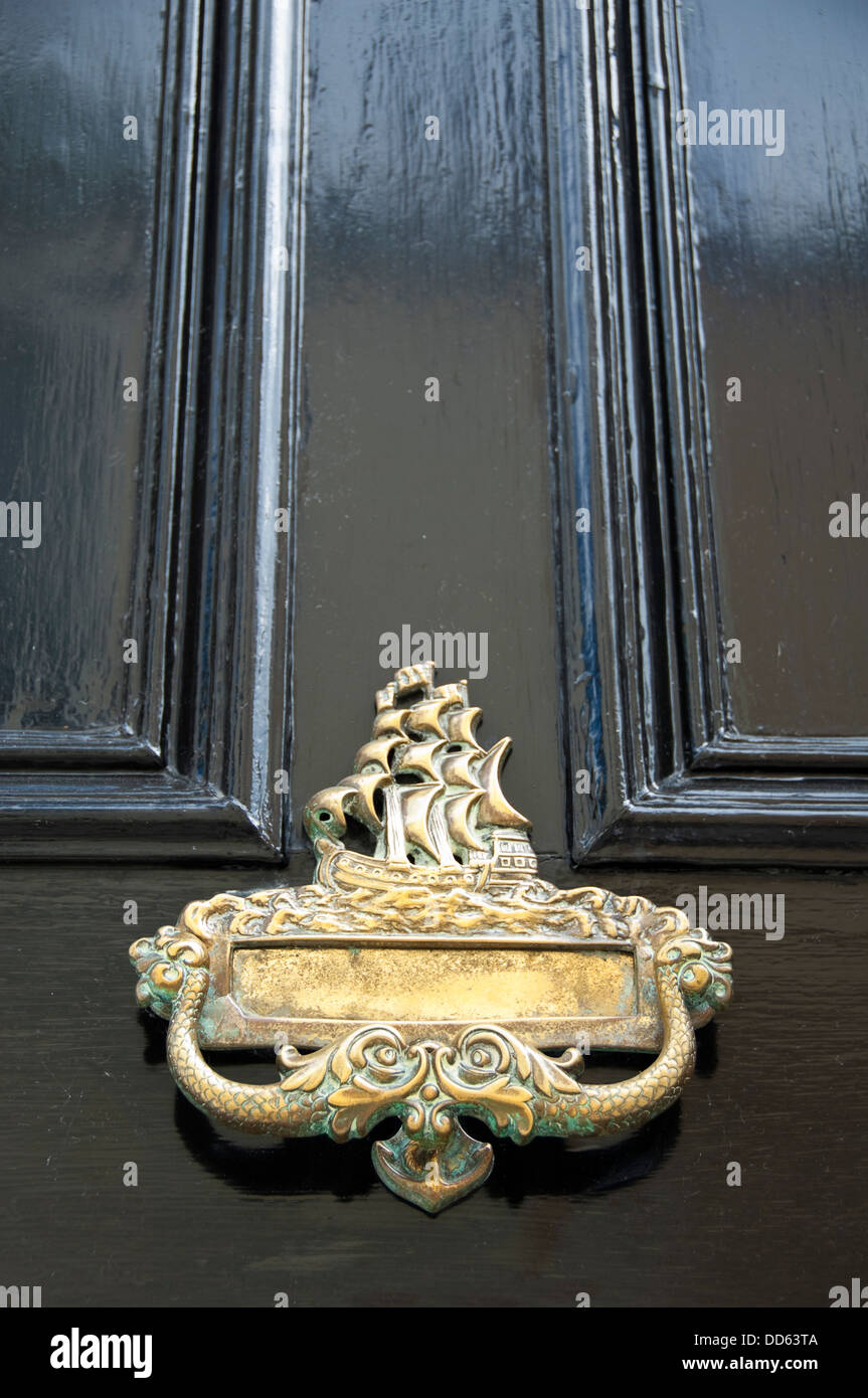 Vertical close up of a large nautical themed brass knocker and letterbox on a black door. Stock Photo