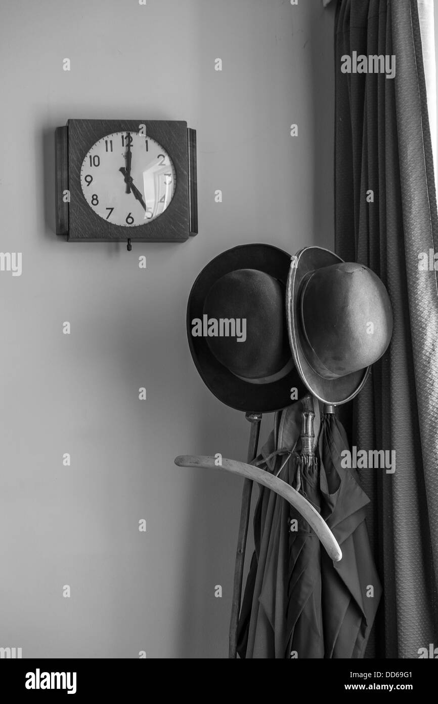 A vintage clock showing 5 o'clock and bowler hats next to umbrellas on a stand Stock Photo