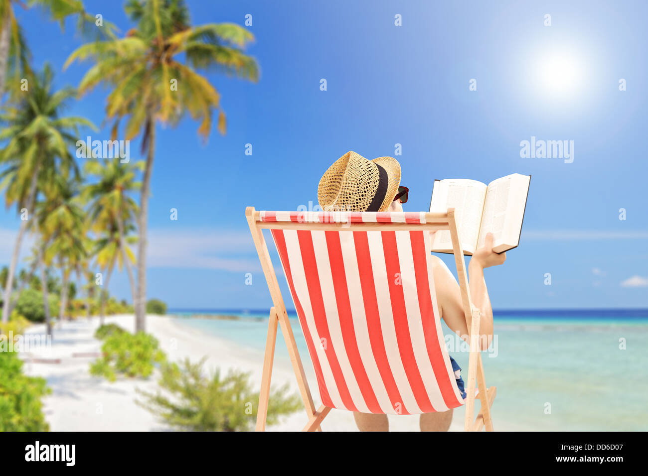 Young man lying on an outdoor chair and reading book, on a tropical beach Stock Photo