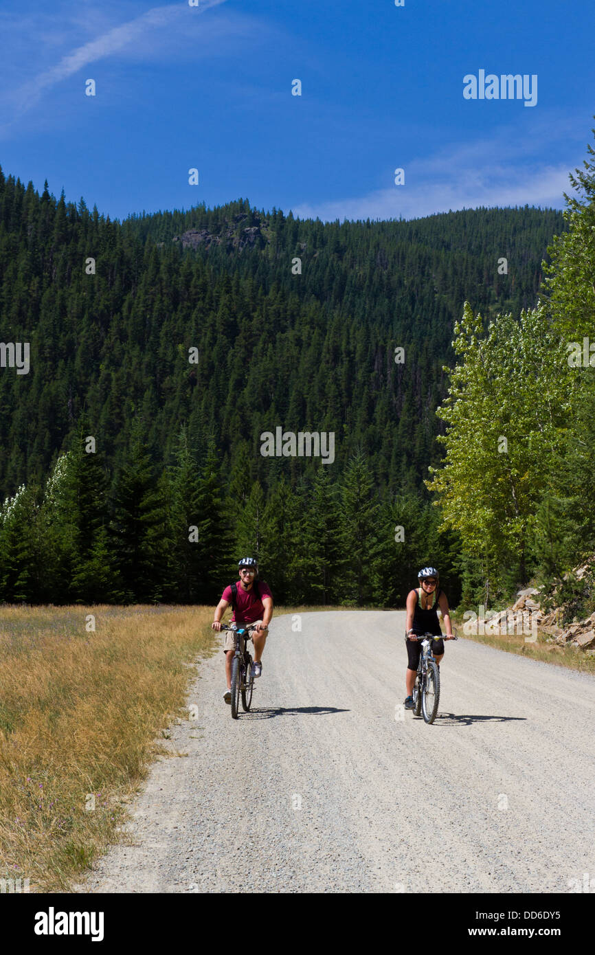 young couple on bicycles riding on a trail thru the mountains of Idaho ...