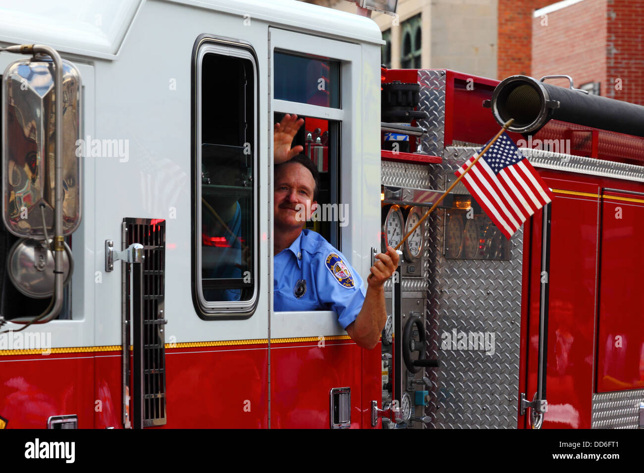 Fireman holding American flag waves while taking part in 4th of July Independence Day parades, Catonsville, Maryland, USA Stock Photo