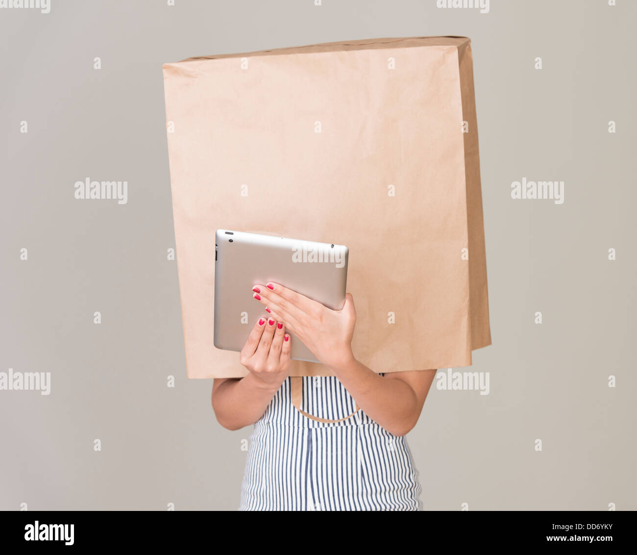 Anonymous internet surfing. Young woman with paper bag over her head holding a tablet Stock Photo