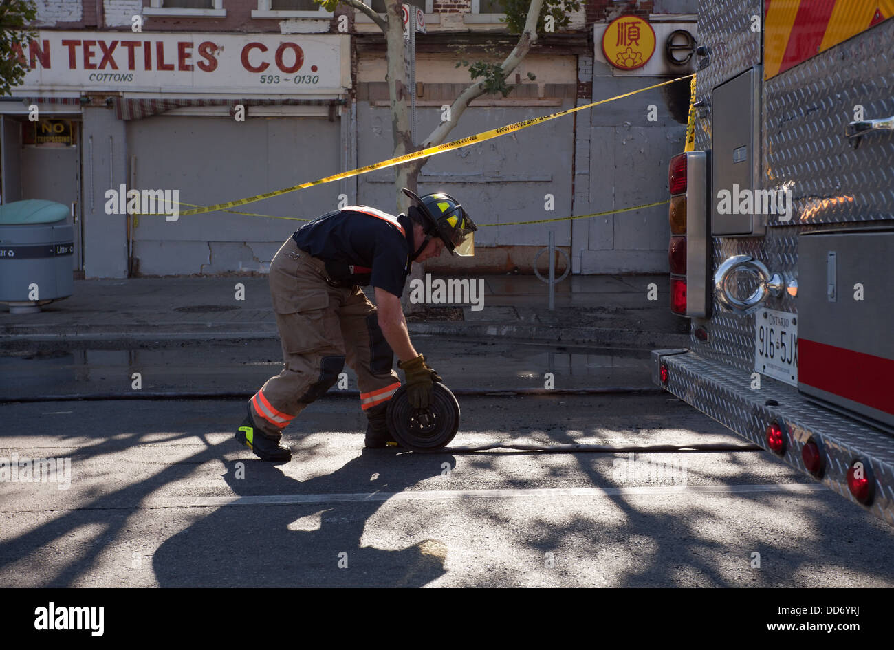 A firefighter rolls up a fire hose after a fire in chinatown, Toronto, Ontario, Canada. Stock Photo