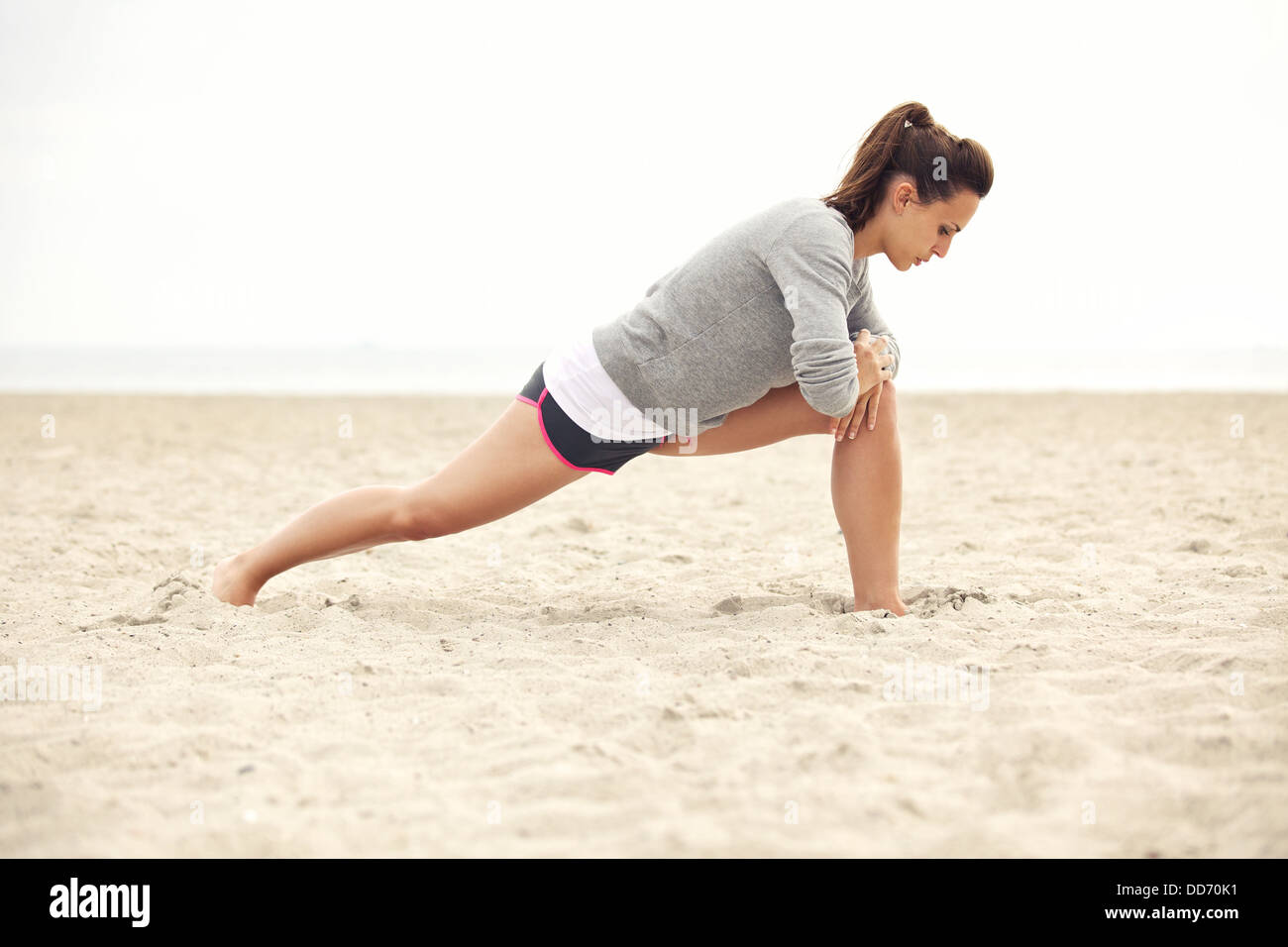 Young female athlete doing stretching exercise on the beach for fitness and a healthy lifestyle. Stock Photo