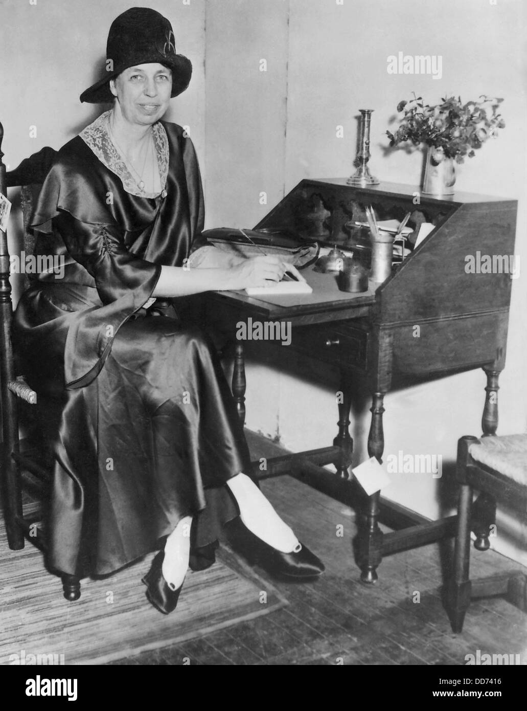 Eleanor Roosevelt in New York City. 1932. She is writing at a desk, dressed in a silk dress with lace collar, cloche hat, and Stock Photo
