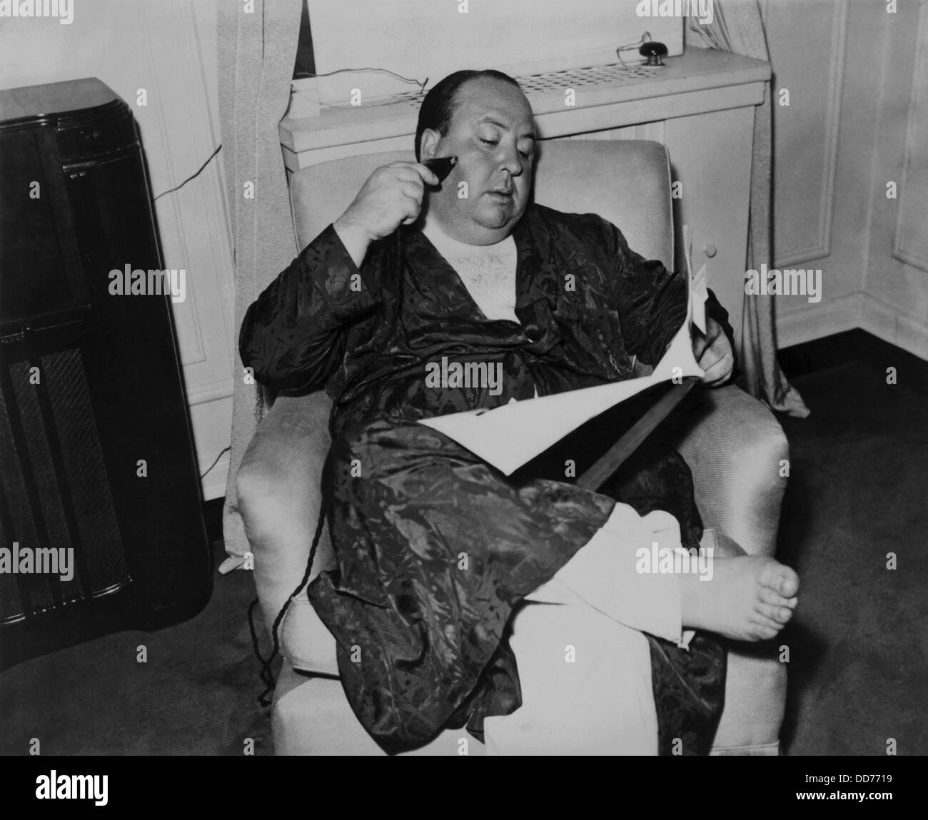 Alfred Hitchcock, seated in a recliner, shaving and reading while in his pajamas and robe, 1938. (BSLOC 2013 8 272) Stock Photo