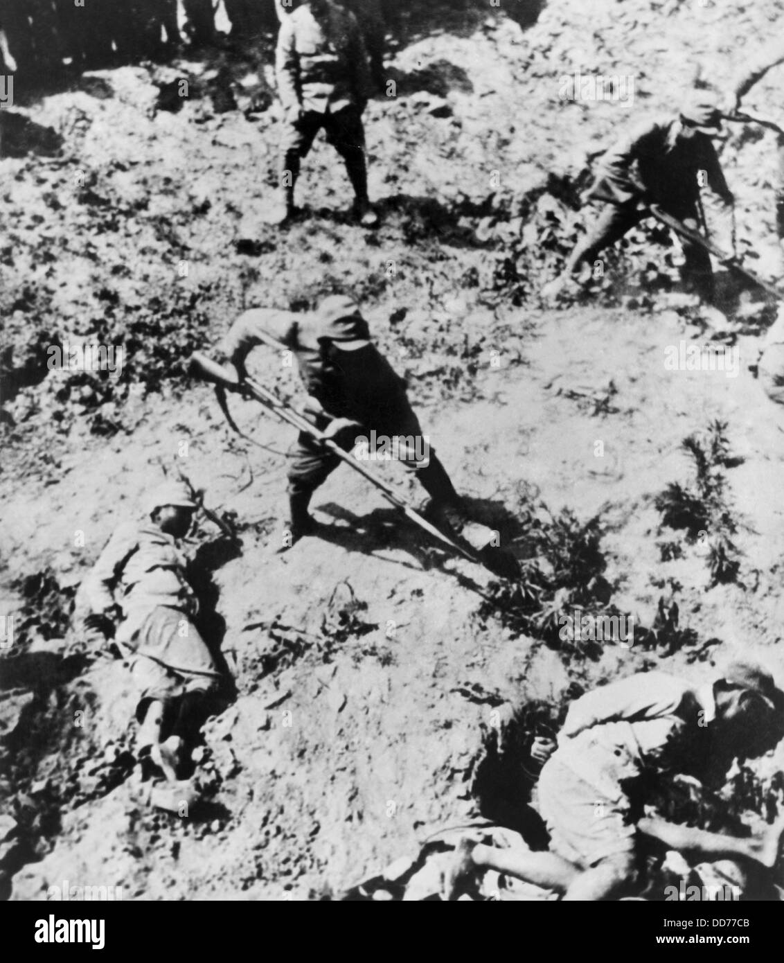 Japanese soldiers with bayonets menacing their Chinese captives. The victims lie on the ground with their hands bound. Between Stock Photo