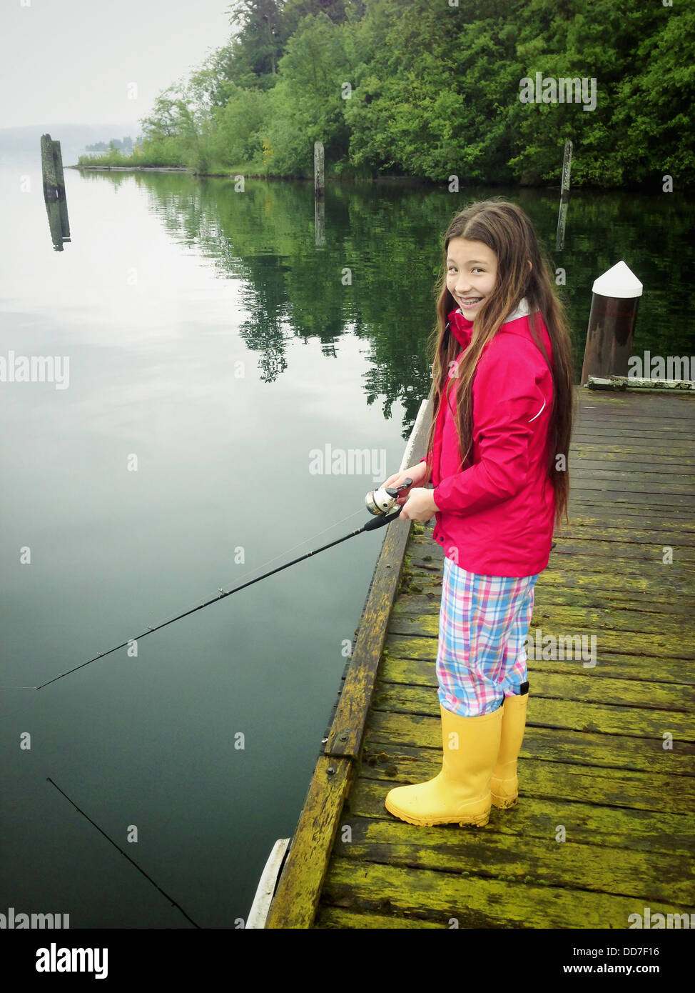 Mixed race girl fishing off wooden dock - Smartphone Captured Stock Image