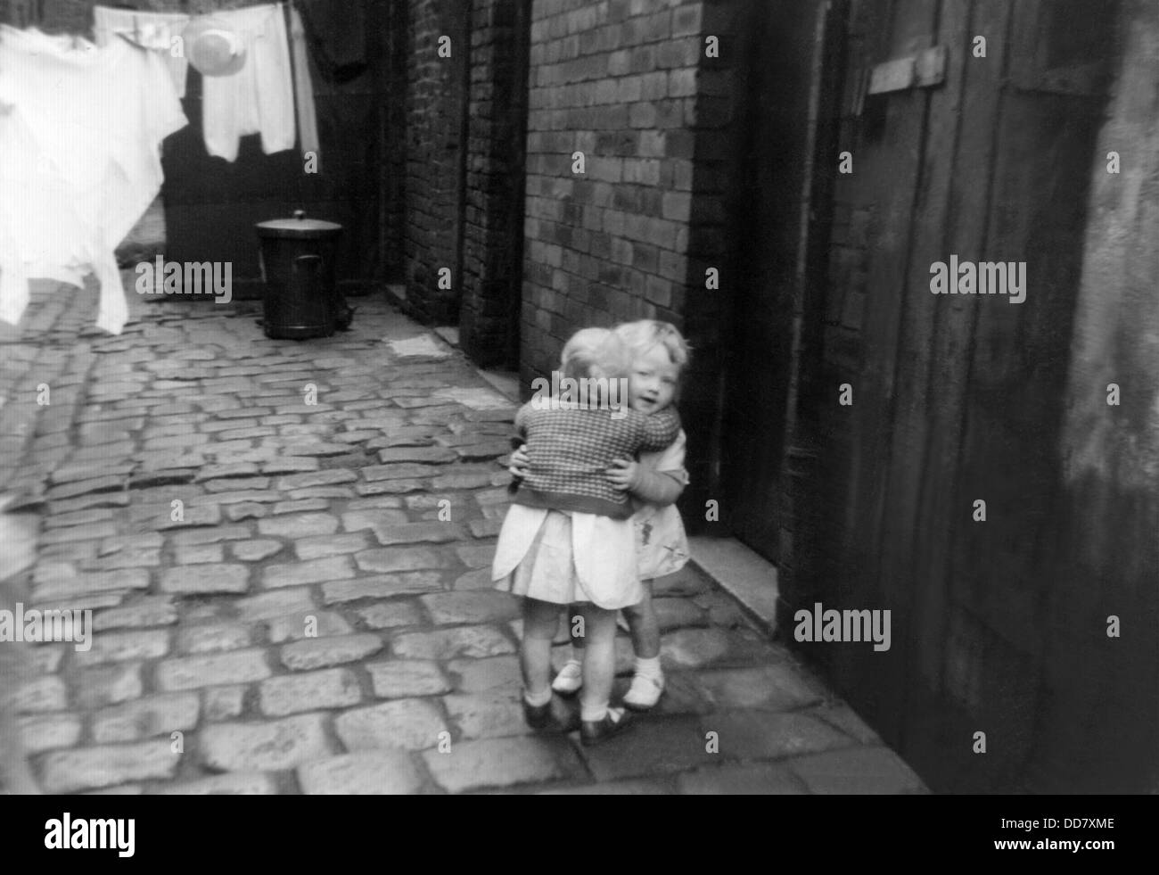 Two young girls hug in the cobbled back street of terraced house in Oldham, Lancashire. Stock Photo