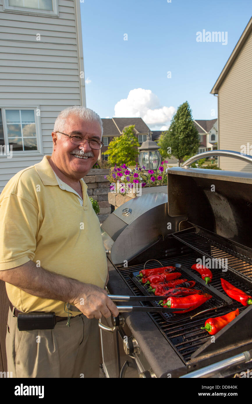 An Old Man wearing a yellow shirt is happily grilling chilies Stock Photo