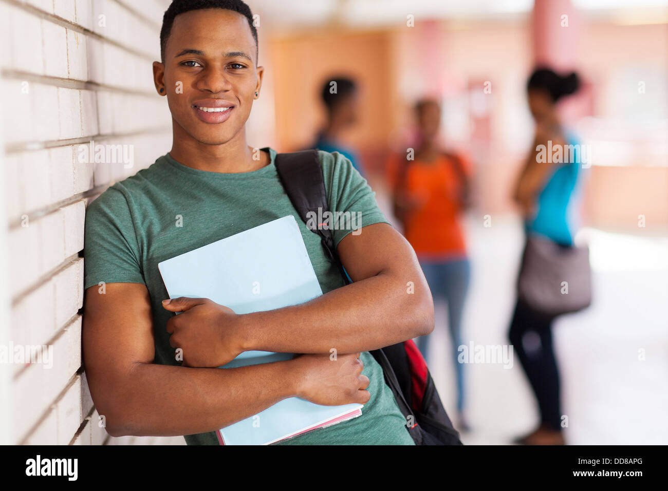 happy African American college student leaning against campus wall Stock Photo