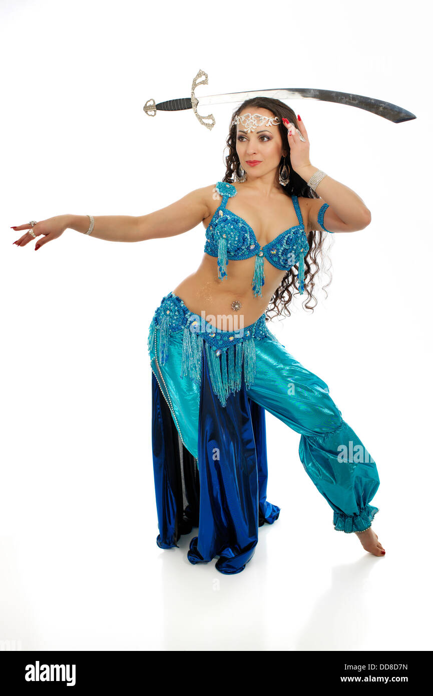 Beautiful professional bellydancer  in colorful costume posing in front of the white backdrop with a sward. Stock Photo