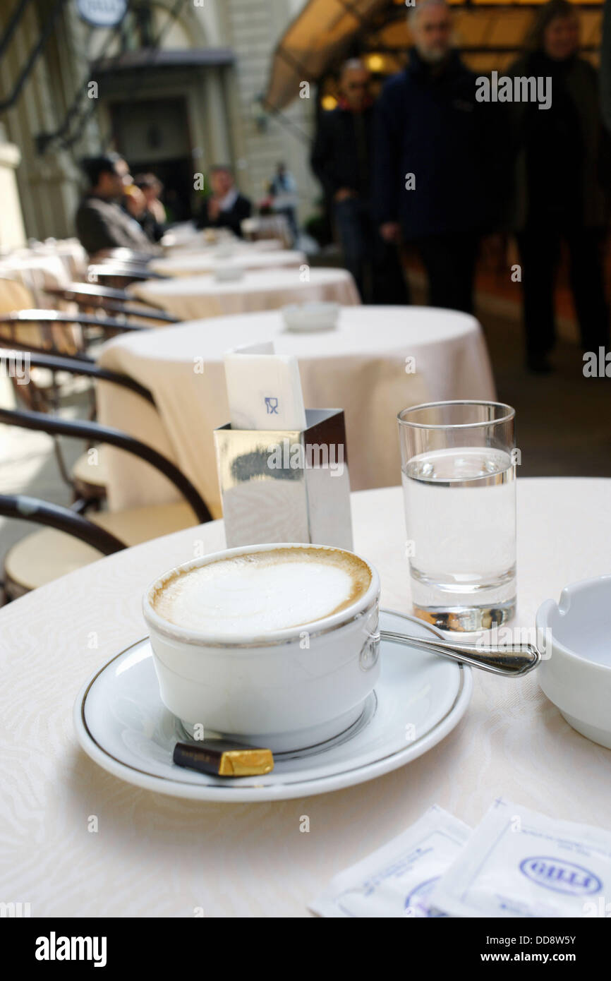 A cup of cappuccino filled with milky foam on a coffee table in a outside café in Florence with a glass of water, sugar bags, Stock Photo