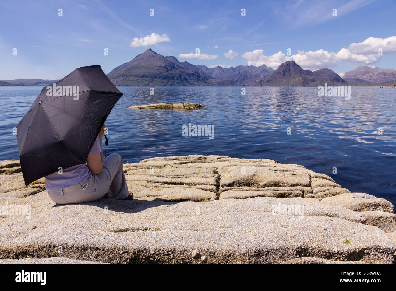 Holidaymaker under sunshade admiring view of Loch Scavaig and the Black Cuillin mountains, Elgol, Isle of Skye, Scotland, UK Stock Photo