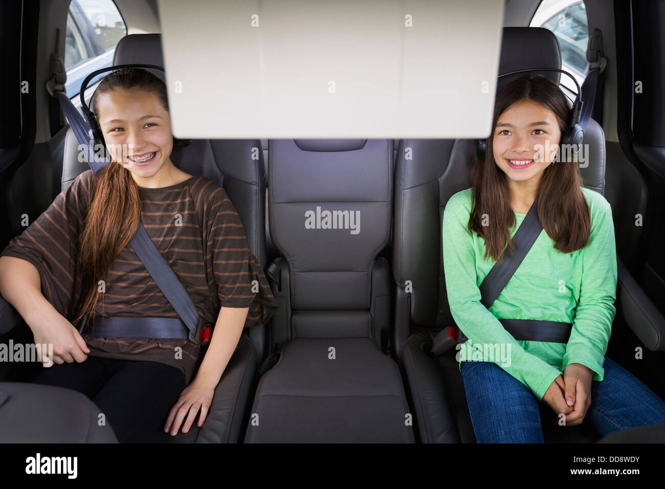 Mixed race girls watching television in backseat Stock Photo