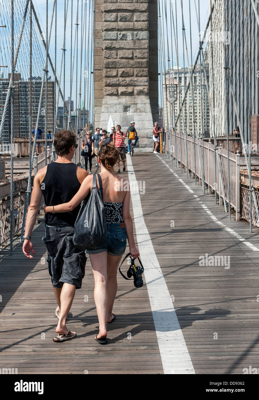 A young couple embracing as they walk across Brooklyn Bridge towards ...