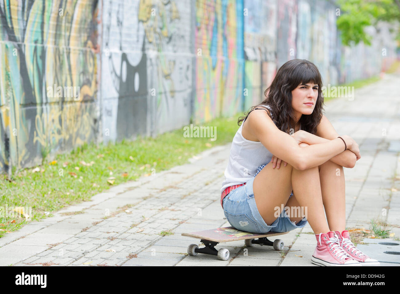 Hispanic woman sitting on skateboard Stock Photo