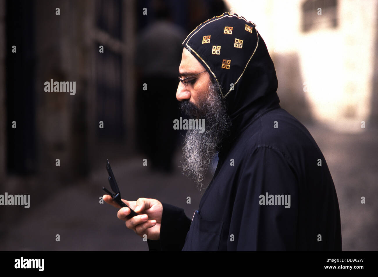 An Assyrian Orthodox Christian priest using mobile phone in the Christian quarter old city of East Jerusalem Israel Stock Photo