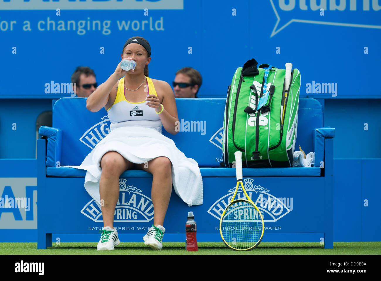 British tennis player Tara Moore takes a drink during the break between games on a blue bench with a towel over her for modesty Stock Photo