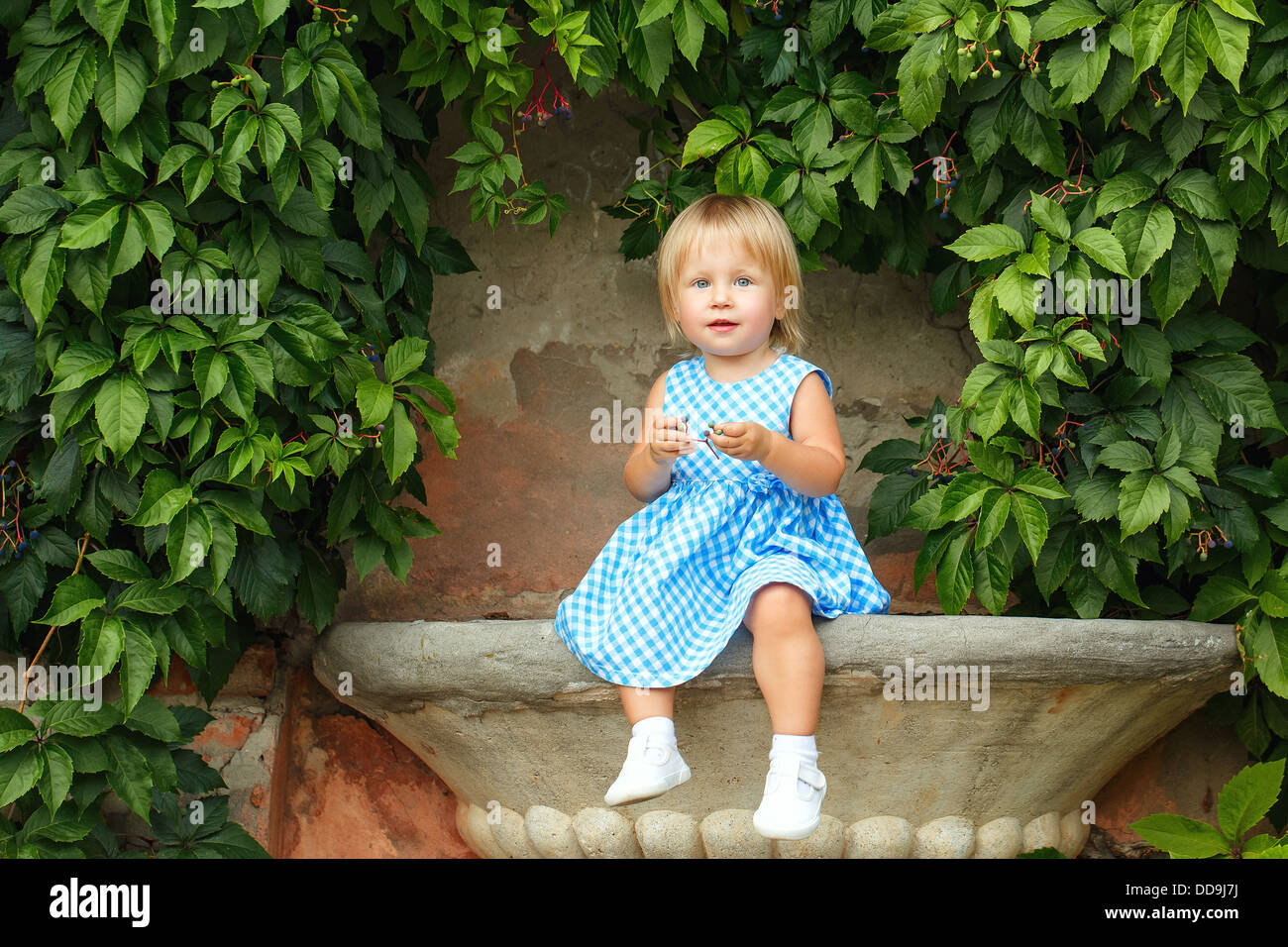 Little blonde girl on a background of green grape leaves Stock Photo