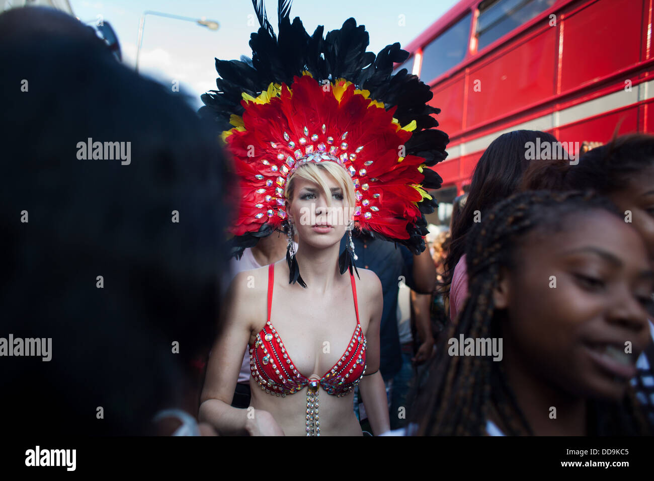 A young white skimpy clad woman makes her way through a crowd of black women along a red double decker bus in the parade. Stock Photo