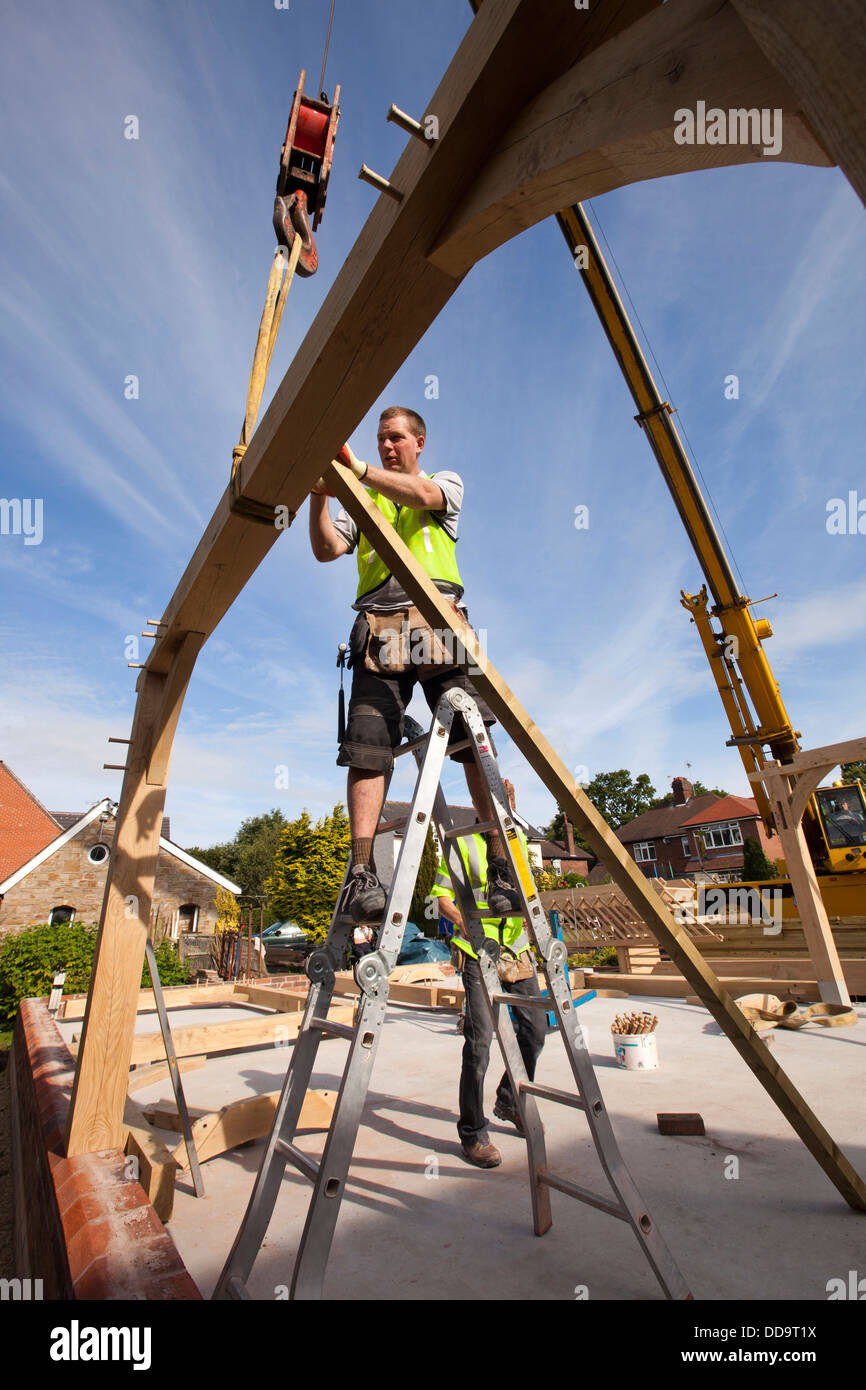 self building house, workers erecting green oak framed buiding with assistance of crane Stock Photo