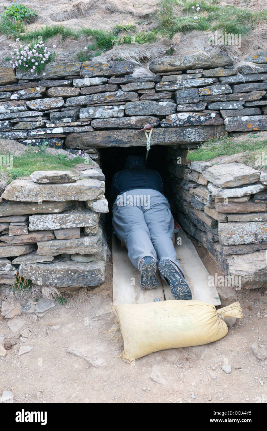 A visitor prepares to enter the Tomb of the Eagles chambered tomb on South Ronaldsay, by means of a wheeled trolley & rope. Stock Photo