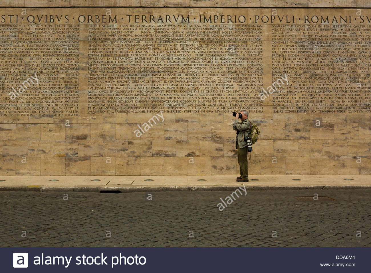 A photographer pauses alongside a engraved wall. Stock Photo