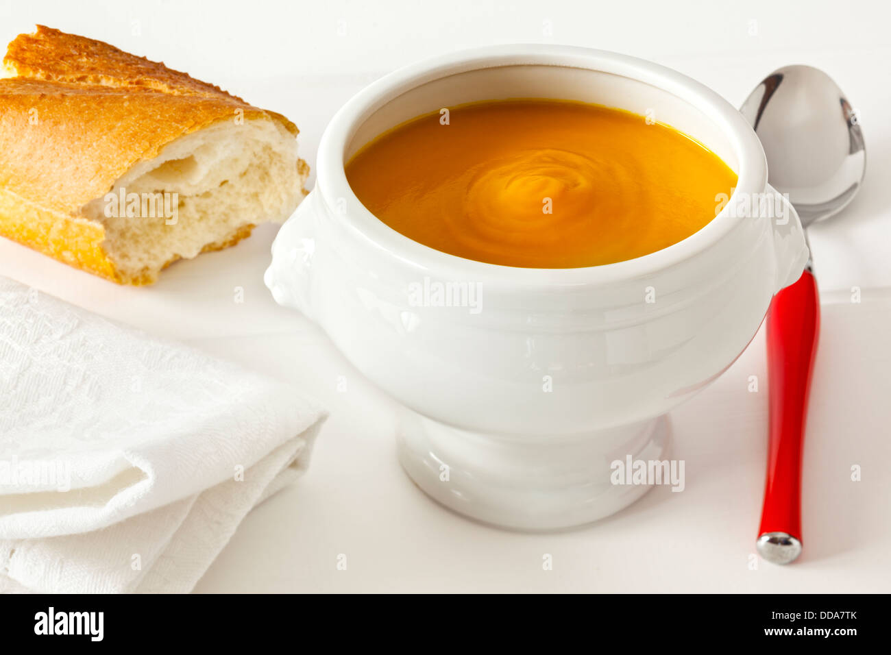 Pumpkin Soup - thick, hearty pumpkin soup served in a lion head bowl with crusty bread, in a light, bright setting. Stock Photo