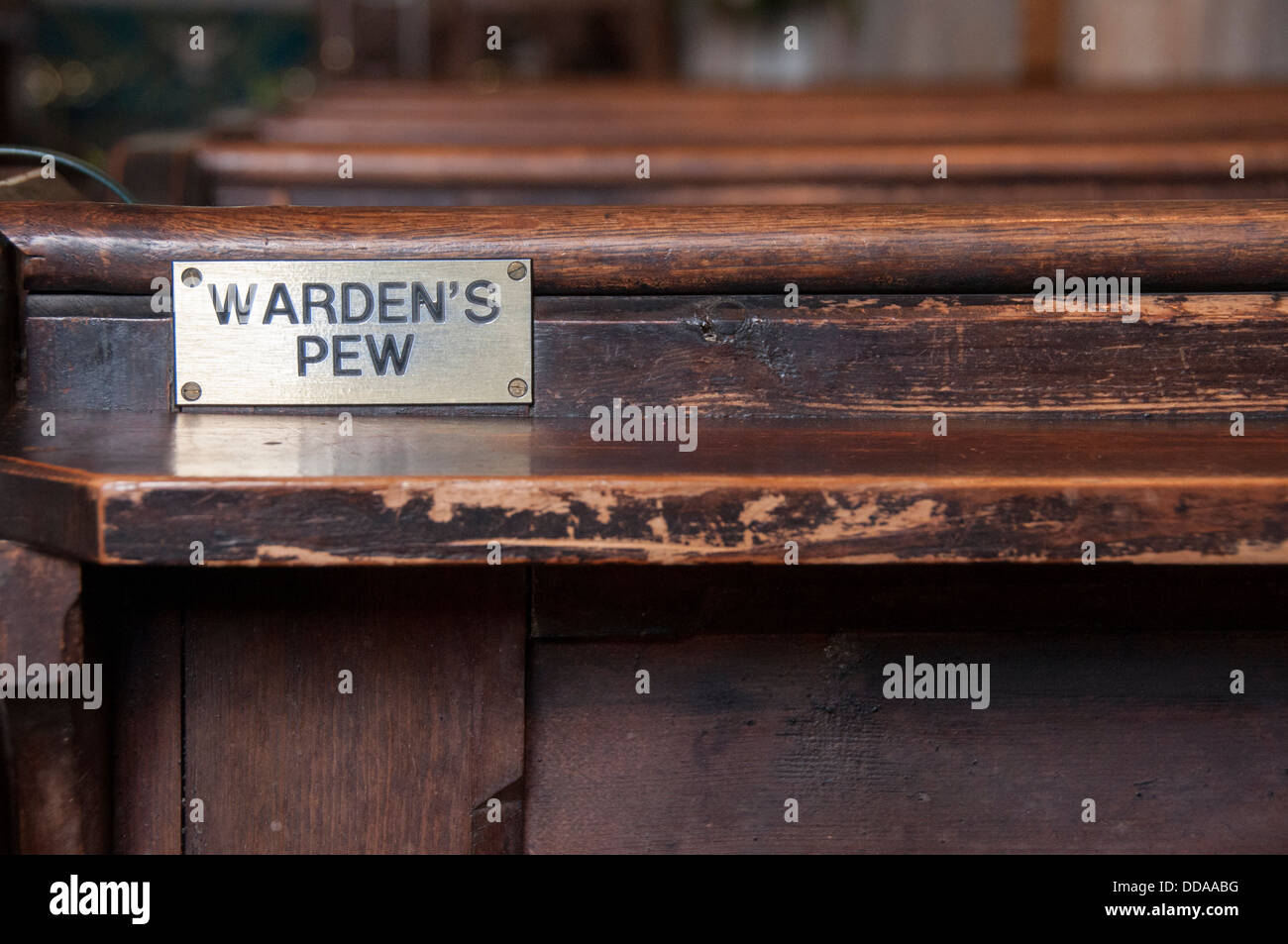 Close-up of metal plaque attached to back of wooden church pew, reading 'Warden's Pew,' a reserved seat for volunteer - Linton Church, Yorkshire, UK. Stock Photo