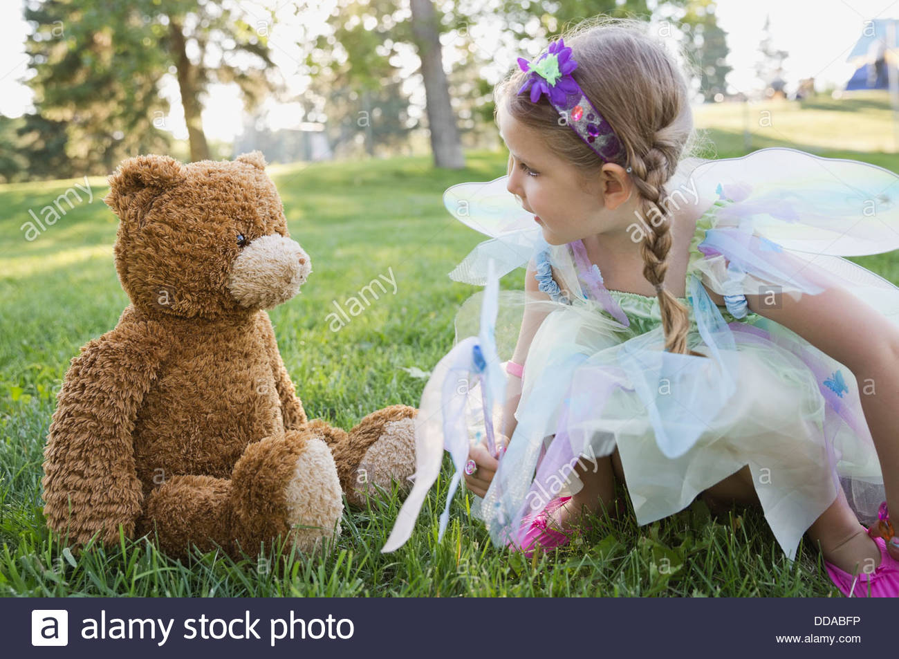 Little girl wearing fairy costume playing with teddy bear Stock Photo