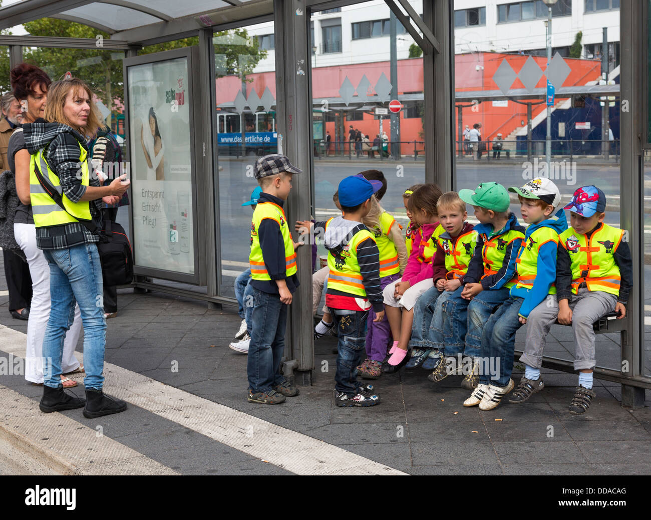 teacher and children at bus stop on field trip wearing fluorescent safety jackets, Potsdam, Germany Stock Photo