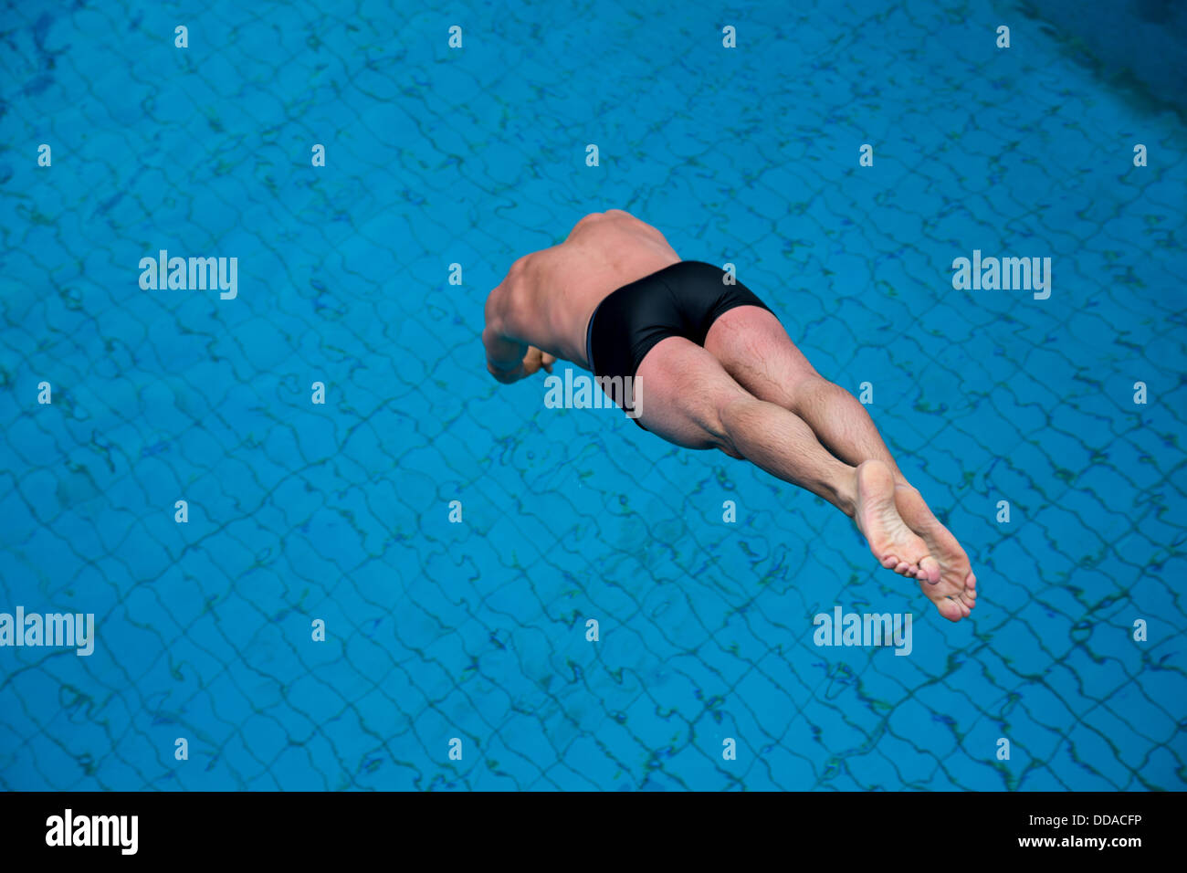 Man jumping from diving board at public swimming pool Stock Photo