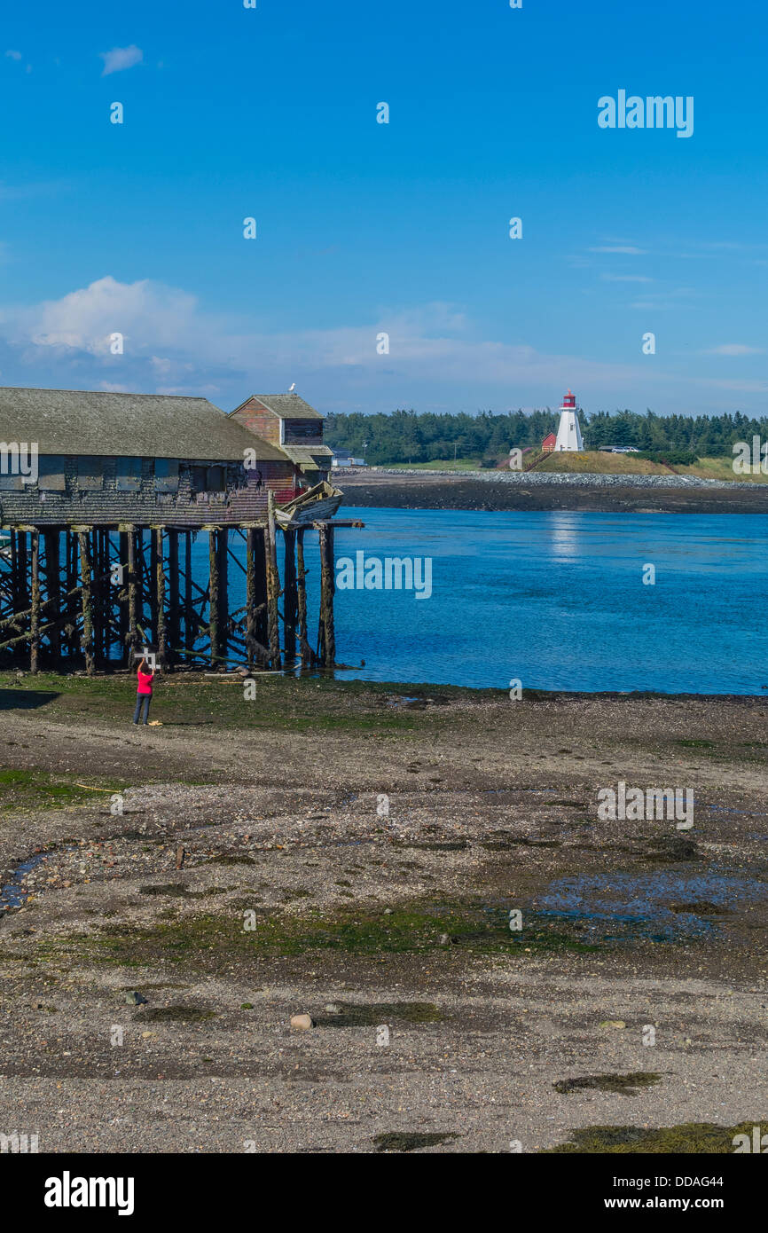 A female artist uses a cropping tool to find the best view of a fish processing building on stilts & lighthouse for a painting. Stock Photo