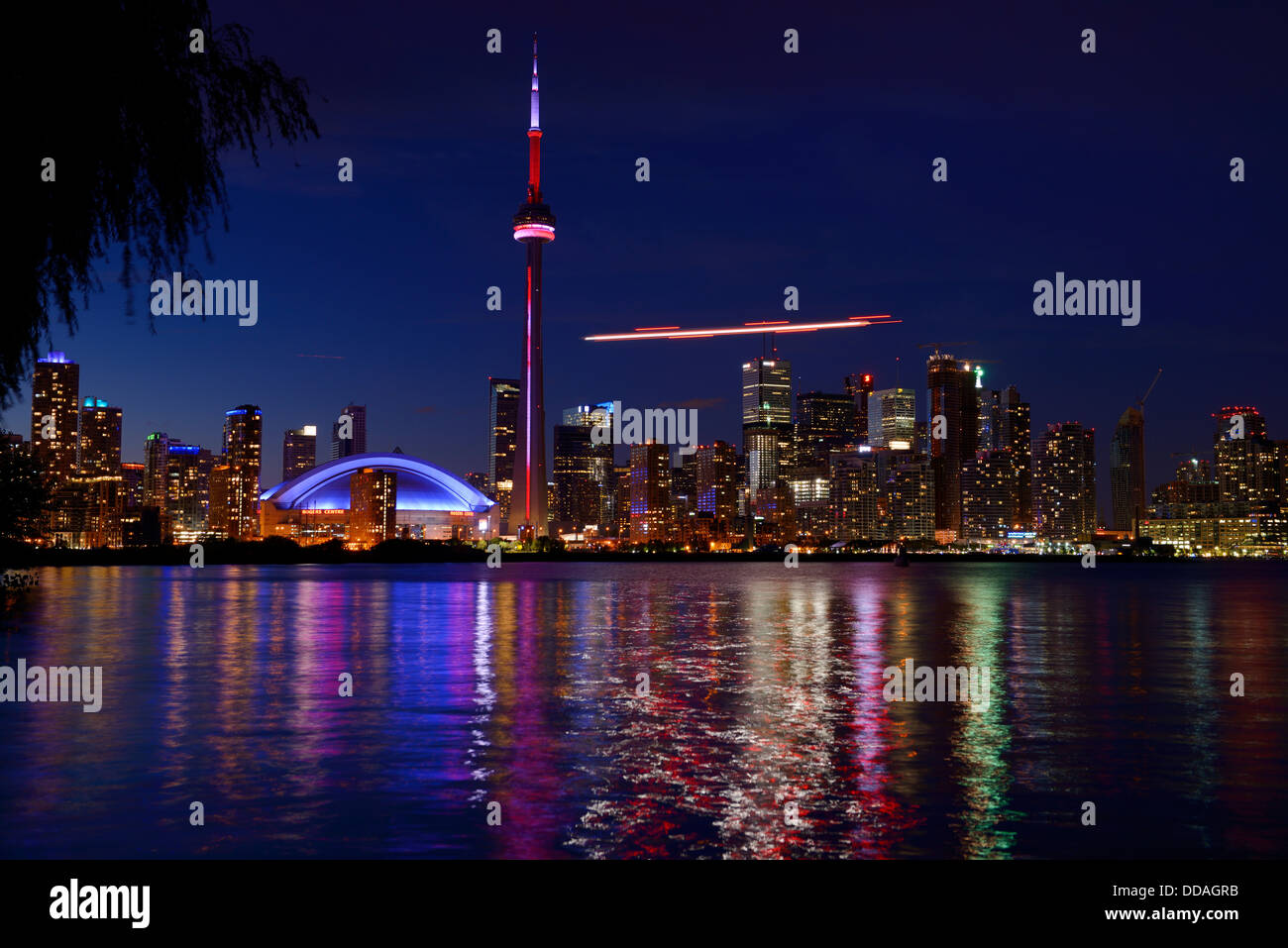 Helicopter landing at the Toronto Island airport with downtown city nightscape skyline with CN tower and Rogers Centre Skydome on Lake Ontario Stock Photo