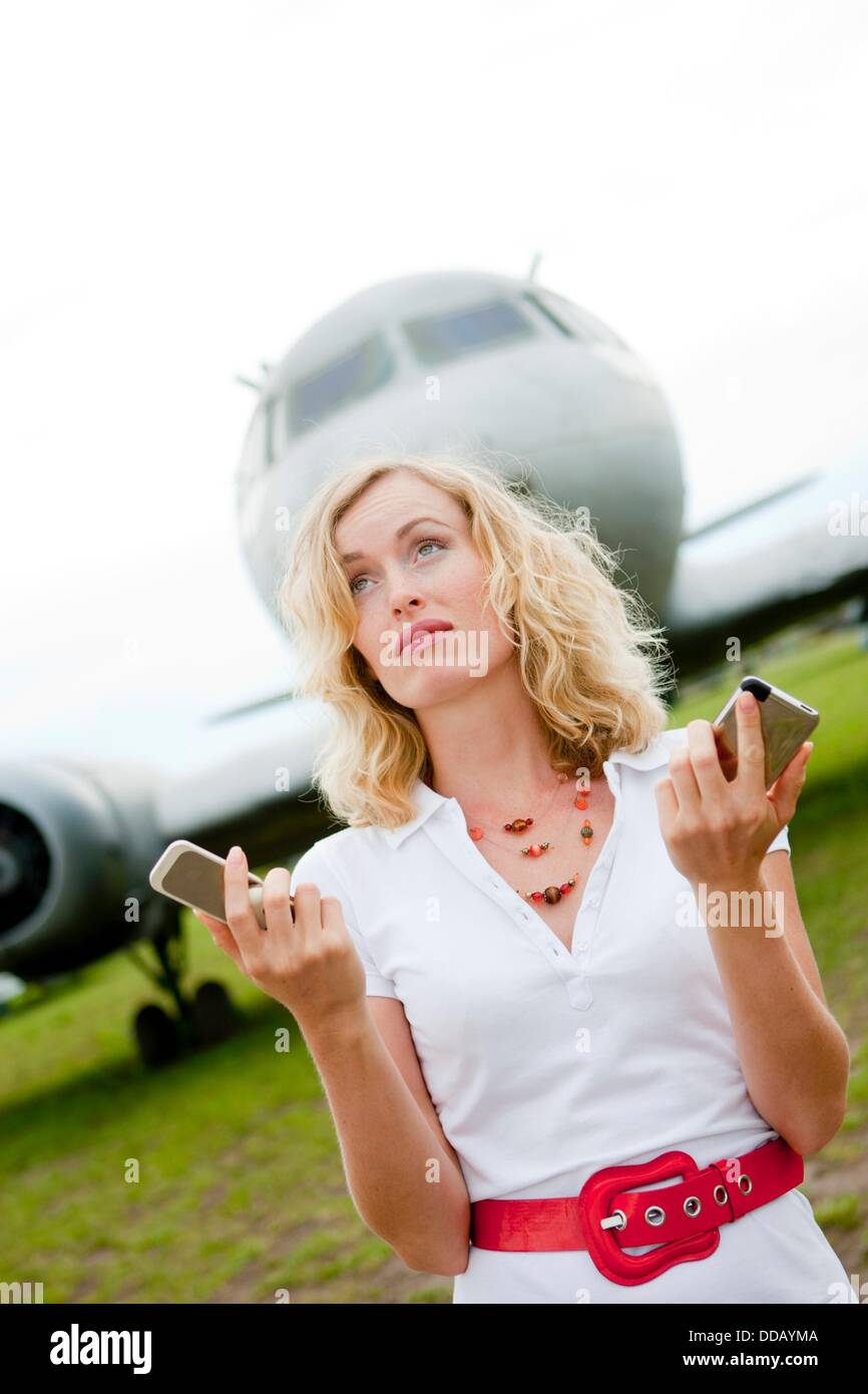A business woman with two mobiles phones next to a plane Stock Photo
