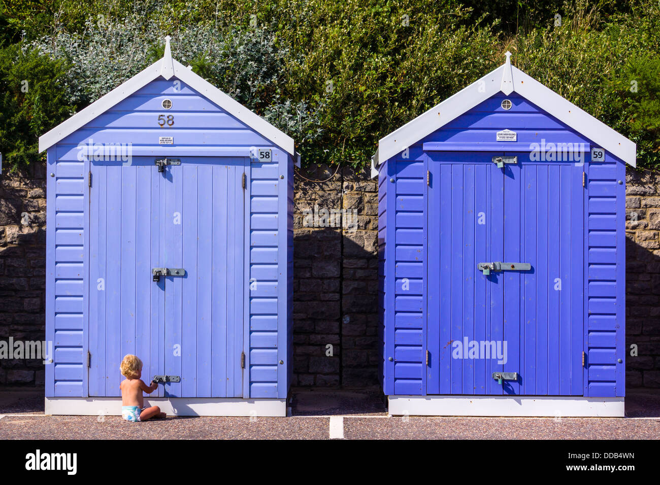 A small child in a nappy plays with the lock to a Beach hut on the seafront in Bournemouth, England. Stock Photo