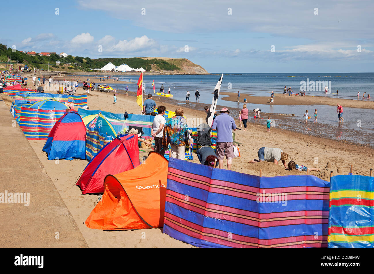 People tourists visitors and colourful tents windbreaks on North beach in summer Scarborough North Yorkshire England UK United Kingdom Great Britain Stock Photo