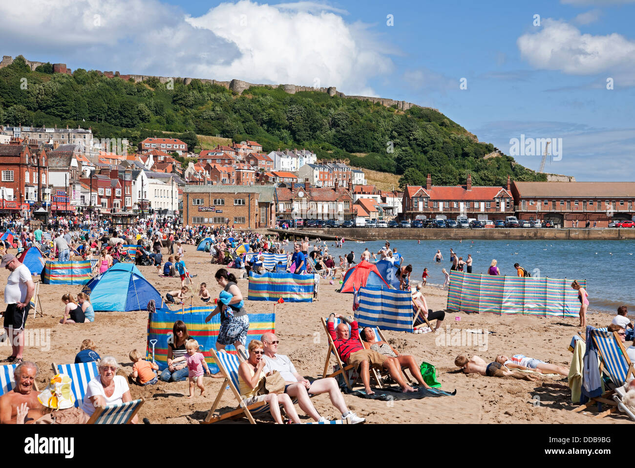 People tourists visitors sitting in deckchairs South Bay beach in summer Scarborough seafront coast resort North Yorkshire England UK GB Great Britain Stock Photo