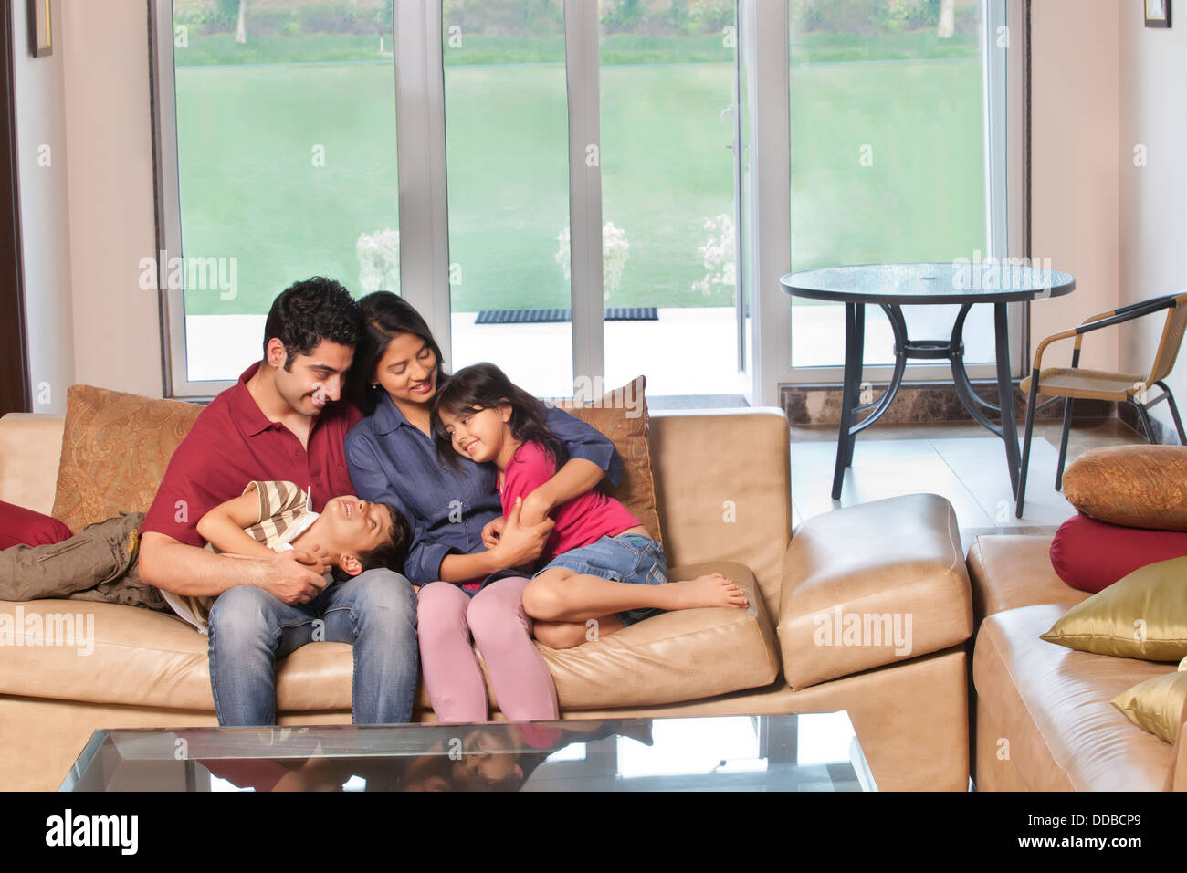 Parents sitting together with kids on sofa at home Stock Photo