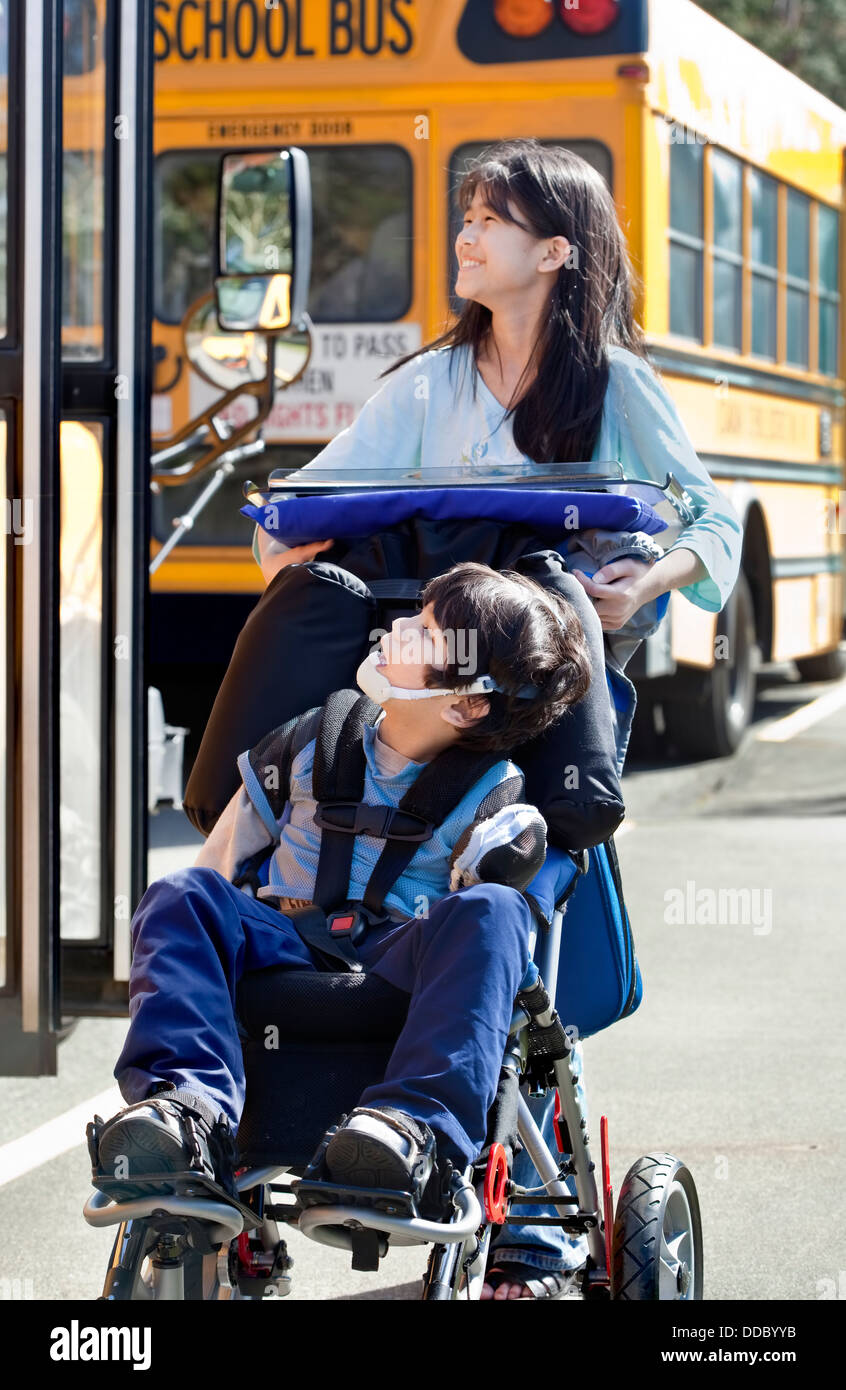 Big sister pushing disabled brother in wheelchair at school Stock Photo
