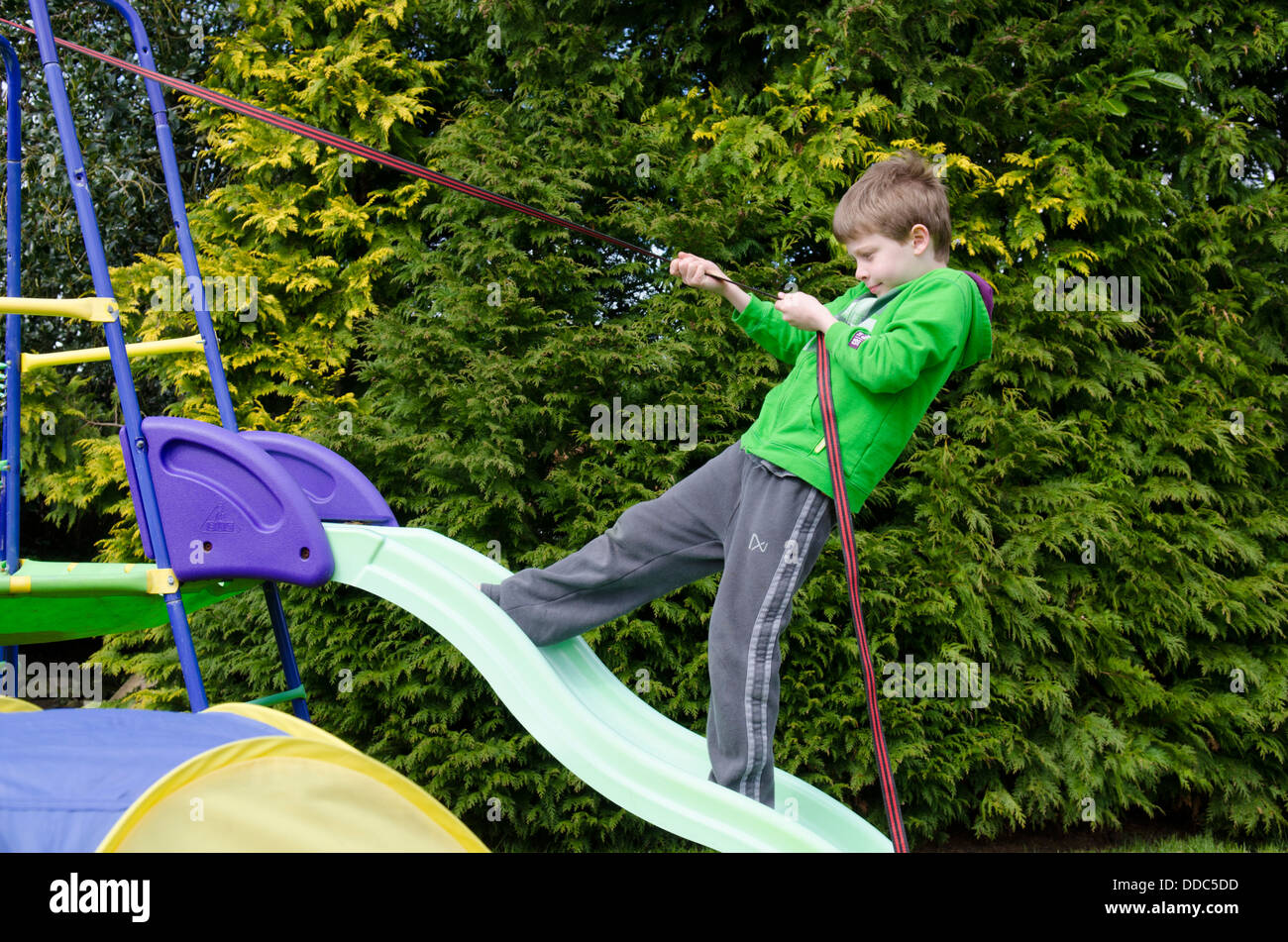 eight year old boy climbing up a garden slide holding a rope or strap