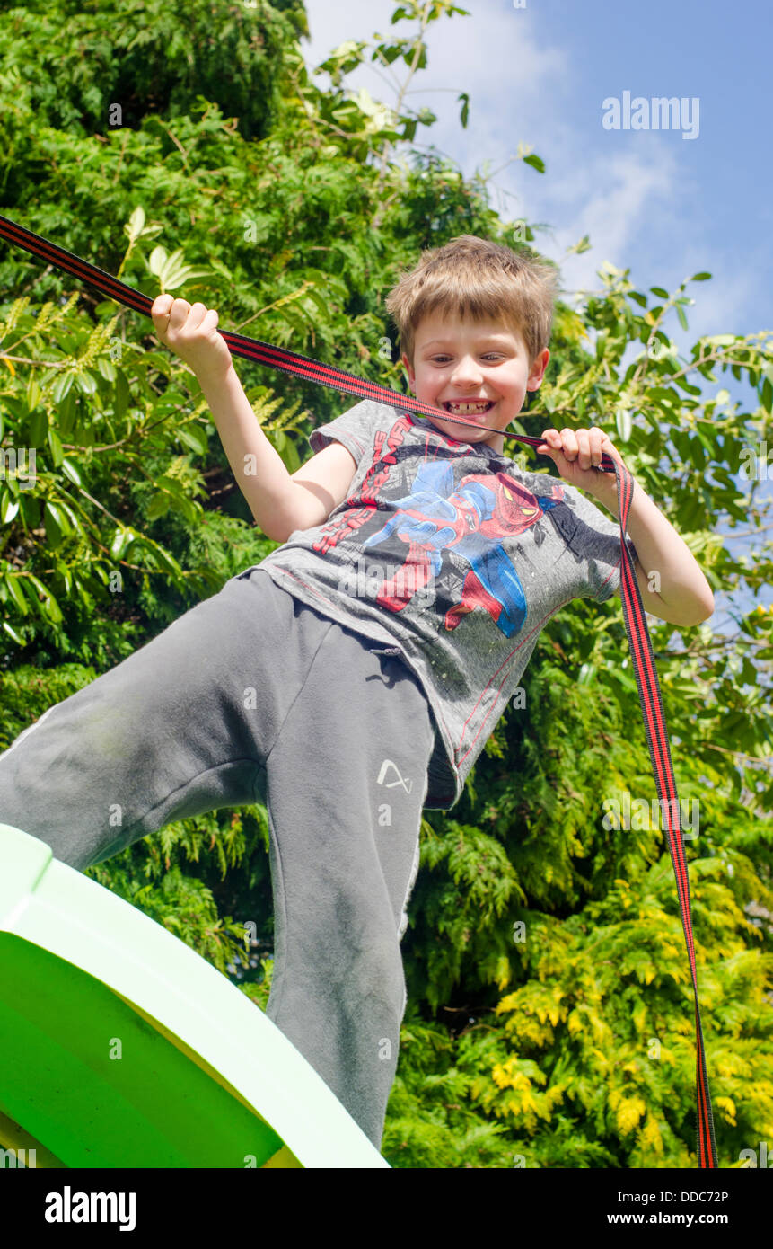 eight year old boy climbing up a garden slide holding a rope or strap that he has tied to the frame Stock Photo