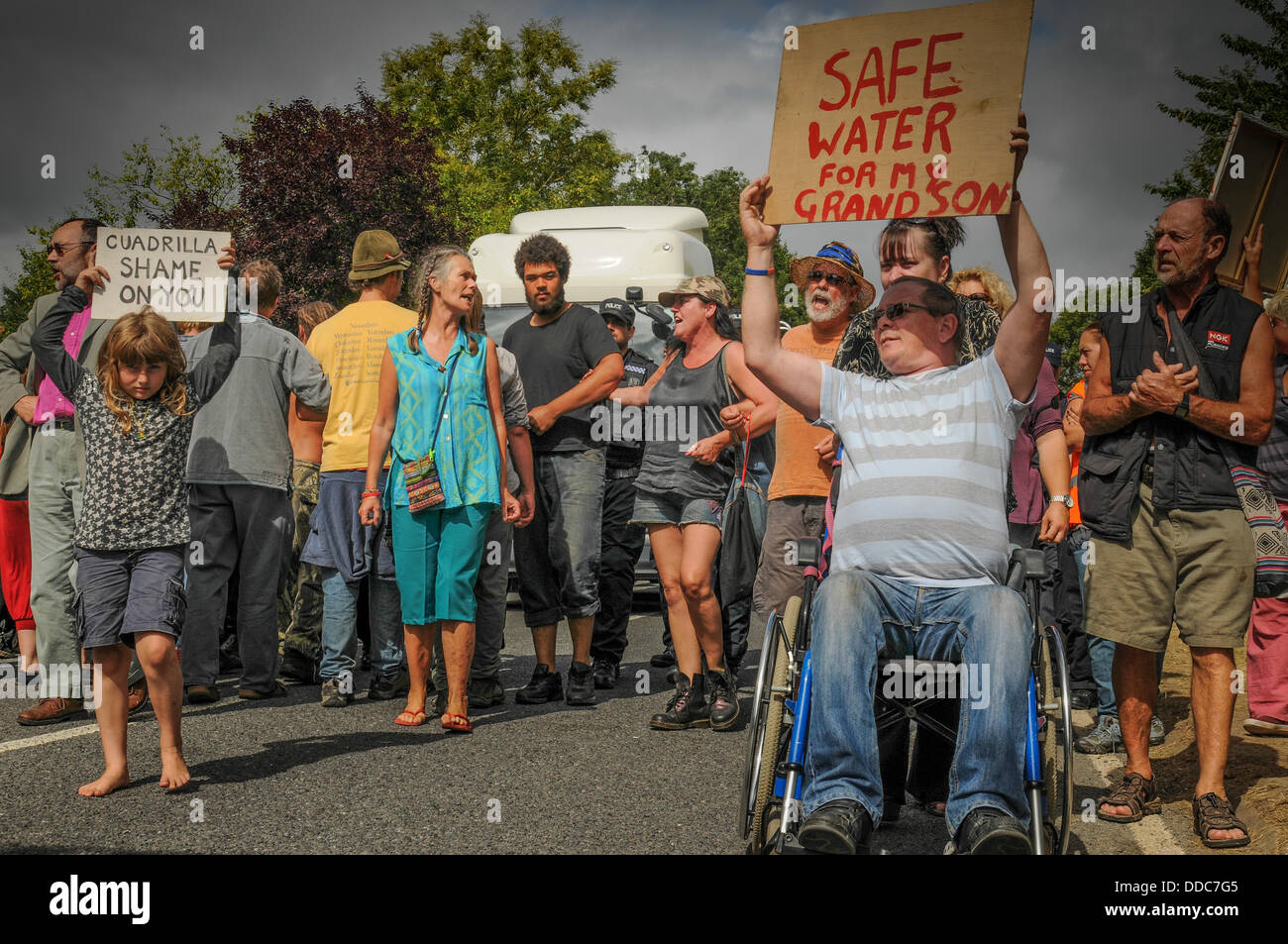 Balcombe, West Sussex, UK. 30th Aug, 2013. Anti fracking environmentalists walk in front as another lorry is escorted to Cuadrilla site by Police. Robin Bothwell, in wheelchair, from Eastbourne on Right makes his point and young girl makes hers. The anti fracking activists are protesting against test drilling by Cuadrilla on the site in West Sussex that could lead to the controversial fracking process. The roadside camp continues to grow. Credit:  David Burr/Alamy Live News Stock Photo